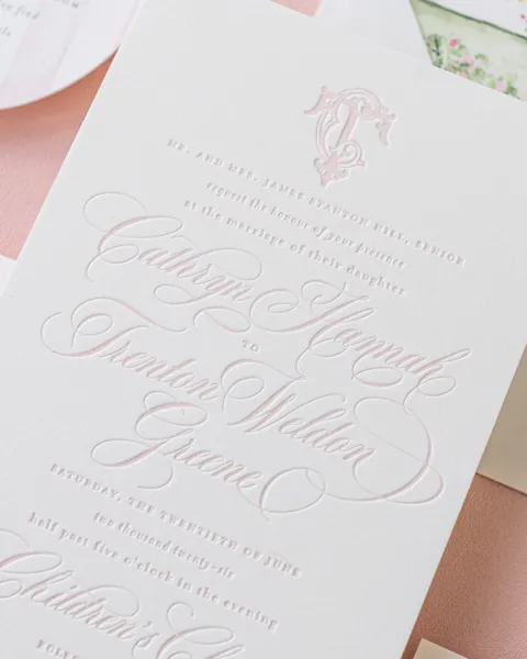 Close-up of pink letterpress Juliette calligraphy on a cotton wedding invitation by Jessica Hinton of Empress Stationery, with a pale pink monogram.
