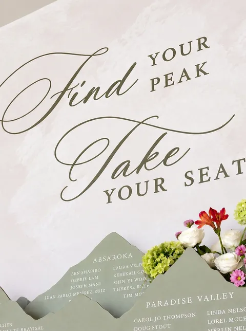 Mountain-themed wedding seating chart by Janeil Anderson of Seventh & Anderson, with olive green lettering, table assignments and fresh flowers.