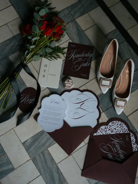 Burgundy and white wedding stationery by Mally’s Crafts, with Juliette calligraphy, scalloped cards, roses and bridal shoes. Photograph by Katie Diana Willcock.