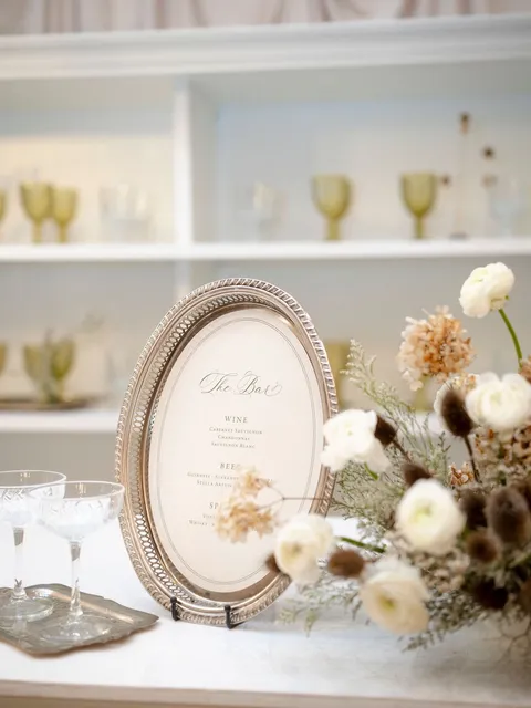Oval framed bar sign by Paper Palette featuring La Rumba calligraphy among glassware and flowers. Design by Tufts & Toile; photograph by Brittany M. Williams.