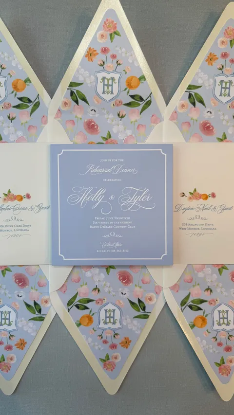 Floral wedding stationery and a blue rehearsal dinner invitation by Claire Hodges Weddings, featuring Mozart Script calligraphy by Blessed Print.