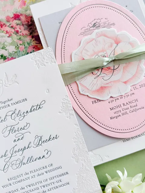 Close-up of La Rumba calligraphy on wedding invitations by Ashley Bunten Design, with a pink oval card, ribbon and hand-drawn floral details.