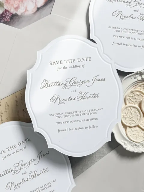 White shaped save-the-date card by Samantha Masterson of Olivean Weddings featuring La Rumba calligraphy and a raised decorative border.