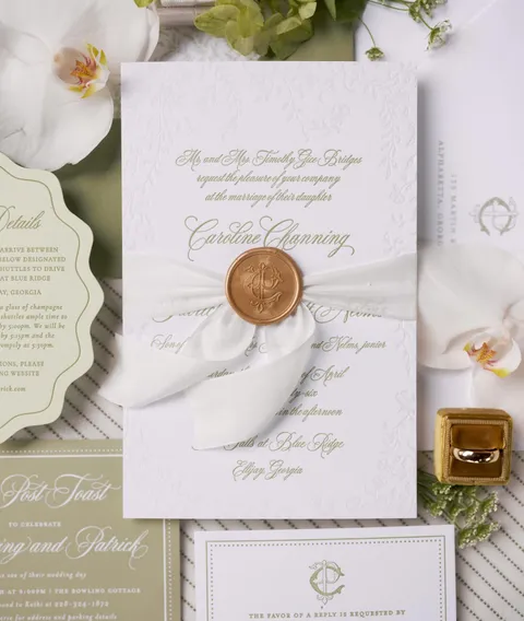 Textured wedding invitation by Sincerely Rachel featuring gold Juliette calligraphy, coordinated green stationery, a wax seal and white flowers.