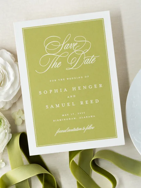 Green and white save-the-date card by Ledgewood Fine Stationery with flowing Juliette calligraphy, styled with green ribbon and white flowers.
