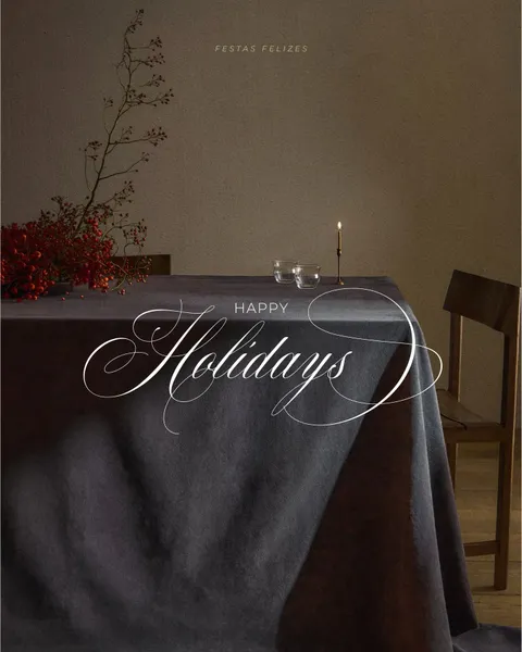 Happy Holidays lettering in white Juliette calligraphy over a softly lit dining table scene by Joana Duarte.