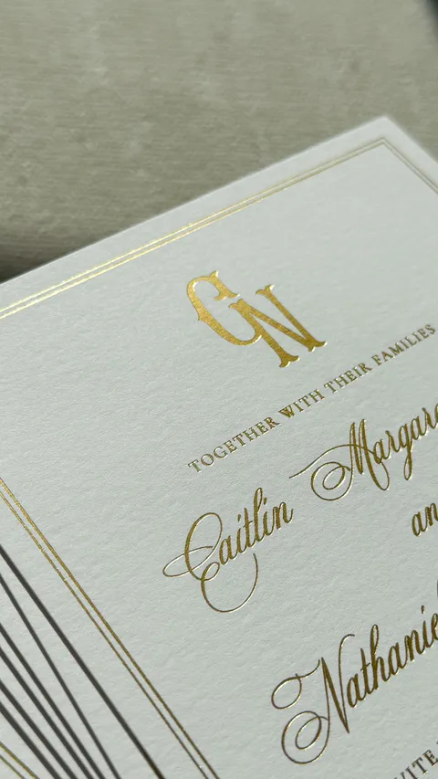 Close-up of a gold foil wedding invitation by Julia Murphy Design Co. featuring Mozart Script calligraphy and a gold monogram.