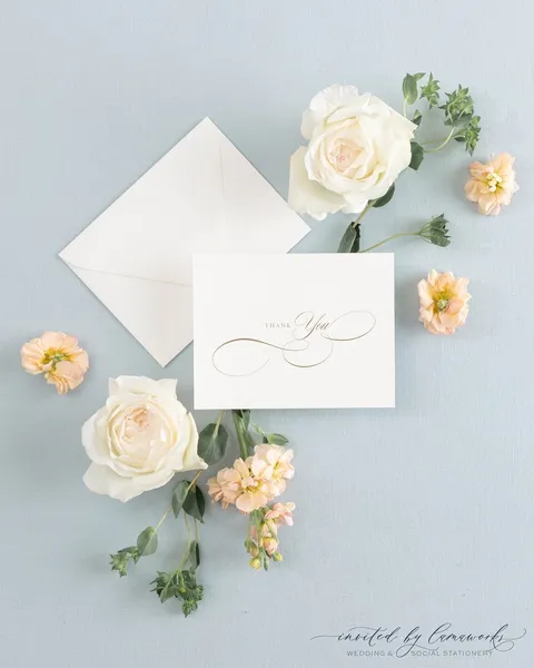 Personalized white thank-you card by Laura Mays featuring gold Juliette calligraphy, styled with a cream envelope and pale flowers.