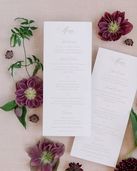 Madison Collection wedding menus by Reverie Paper Co. with Mozart Script headings, styled with burgundy flowers. Photograph by mmmols.