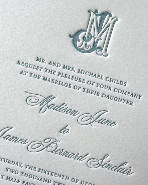 Letterpress wedding invitation close-up by Julia Murphy Design Co. featuring Mozart Script names and an embossed blue monogram.