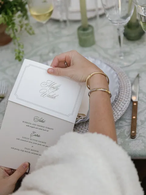 Guest holding an engagement party menu by Ivy & Linen Design with Juliette calligraphy at a floral tablescape. Photograph by Anya Kernes.