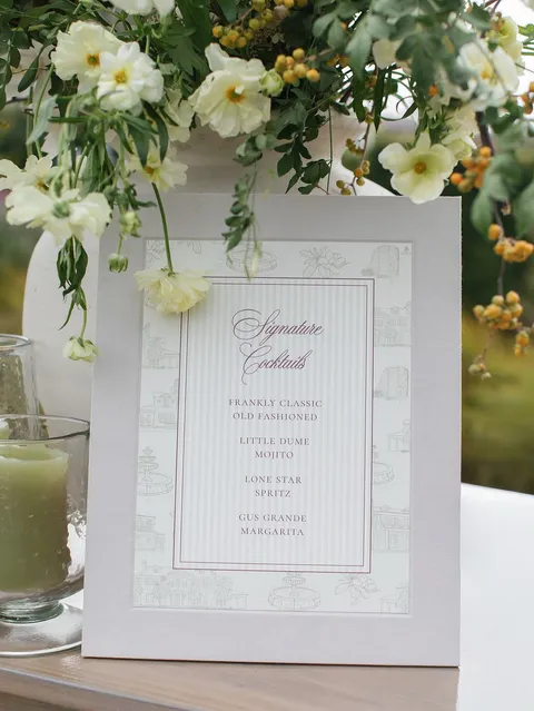 Framed engagement party menu by Ivy & Linen Design featuring Juliette calligraphy, surrounded by white flowers and greenery. Photograph by Anya Kernes.
