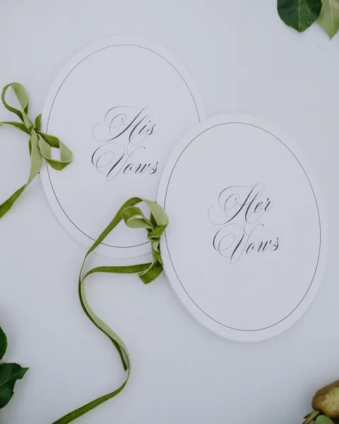 White oval His Vows and Her Vows books from the Lovelle Collection by Mally’s Crafts, with Juliette calligraphy and green ribbon. Photograph by Images by Anna.
