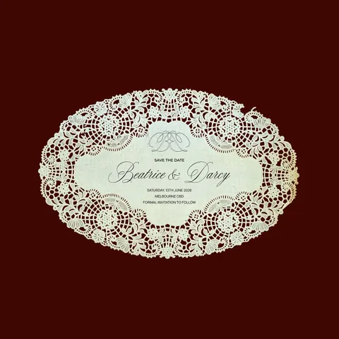 Vintage-inspired oval invitation by Alexandra Collins with Juliette calligraphy, intricate lace edging and a monogram on a burgundy background.