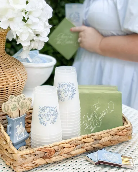 Wedding cups and green can coolers by Empress Stationery with floral artwork and white Juliette calligraphy, arranged on a woven tray.
