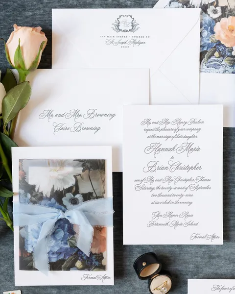 Wedding invitation suite by Banter & Charm with black Juliette calligraphy, a floral vellum wrap and soft blue silk ribbon. Photograph by Sarah Sage Photography.